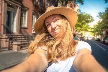 Young happy woman tourist making selfie photo with beautiful view. Blonde tourist girl taking selfie while walking outdoors on city street.