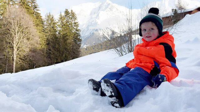 Boy in winter outfit play with snow at mountains on background