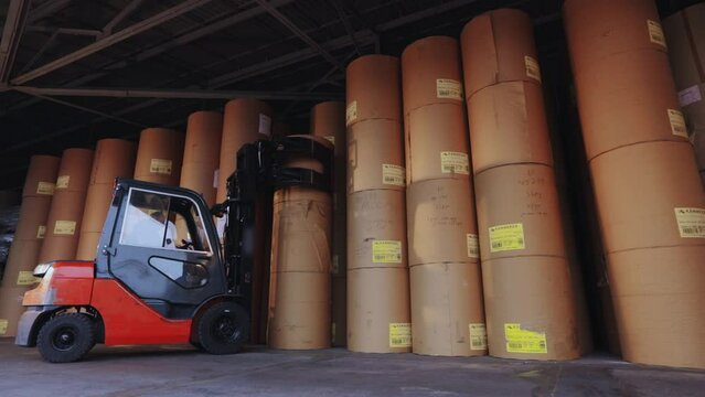 The forklift is carrying a large roll of paper. A forklift is carrying paper at the factory. Loader at the wallpaper factory