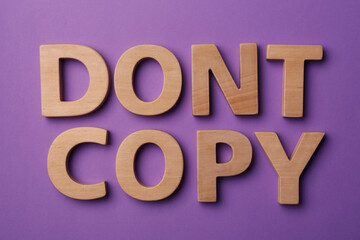 Plagiarism concept. Phrase Don't Copy made of wooden letters on violet background, top view