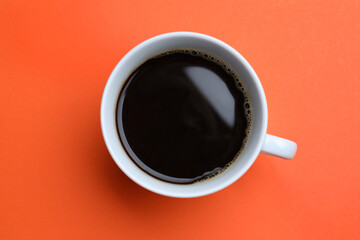 White mug of freshly brewed hot coffee on orange background, top view