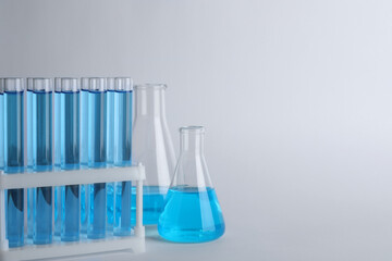 Laboratory glassware with blue liquid on light grey background. Space for text