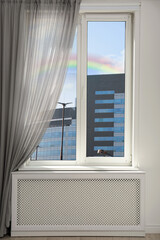 View of beautiful rainbow in blue sky through window