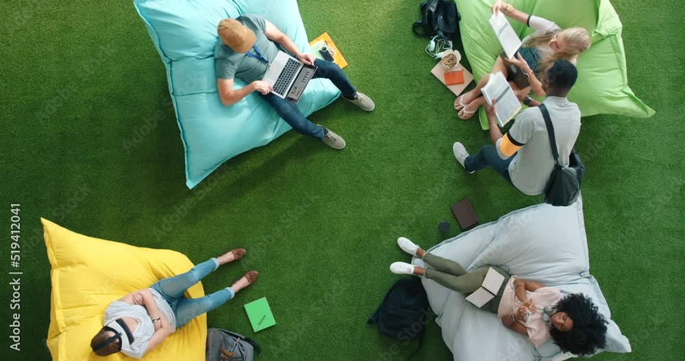 Poster students using technology and sitting on bean bags in a library from above. bright informal office s