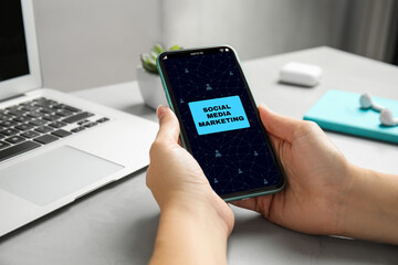 SMM (Social Media Marketing) concept. Woman using smartphone at table, closeup