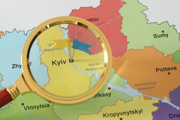 Map of Ukraine with yellow and blue flag push pins placed on Kyiv, view through magnifying glass