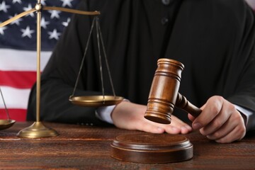 Judge with gavel at wooden table near flag of United States, closeup