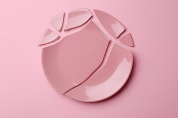 Pieces of broken ceramic plate on pink background, flat lay