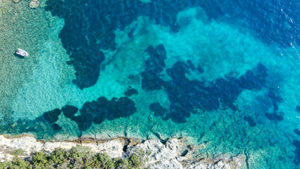 Aerial view of calm turquoise sea water and rocks from molten lava from drone. Pattern of sea surface and rocky shore. Sea, Greece. Rocky coast of the peninsula