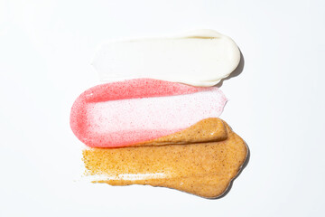 Face scrub creamy texture. White, pink and brown natural cosmetic exfoliation cleanser smear smudge isolated on white. Facial mask sample. Spa treatment, skin care routine
