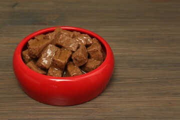 Wet pet food in feeding bowl on wooden background, space for text