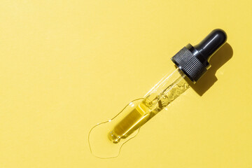Bottle pipette dropper with liquid yellow retinol or vitamin c gel or serum on a yellow background. Skin care smear