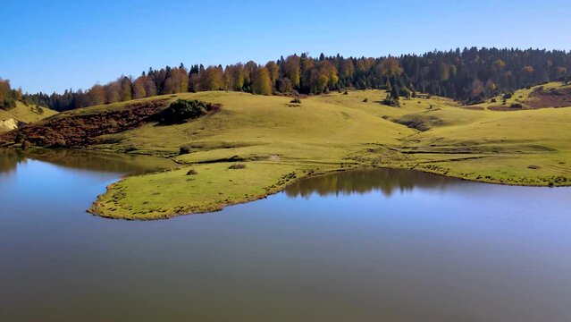 Aerial low height footage of green plateau with lake, hills and trees on the hills in autumn, reflections of trees and sky, afternoon, no people and no houses, Sultanpinar Plateau Sakarya Bolu Turkey