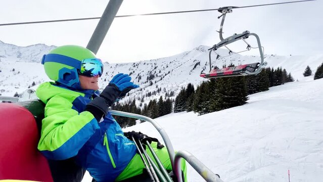 Skier boy on the chair lift put hands up and smile