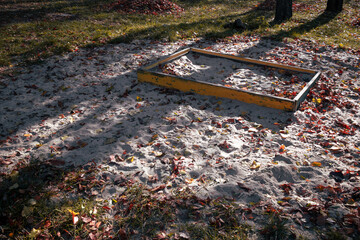 Old abandoned sandbox covered with autumn leaves. Empty and dirty sandbox in an abandoned playground