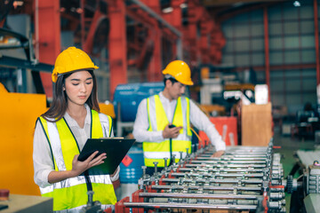 Happy professional beautiful Asian woman industrial engineer/worker/technician with safety hardhat use clipboard to inspect quality control of machinery in production steel manufacture factory plant