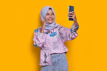 Fototapeta na wymiar happy young asian beautiful muslim woman using mobile phone isolated on yellow background 