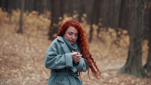 Young Red-haired Woman Freezes in Autumn Park. Female Trying To Keep Warm In Cold Outdoors.