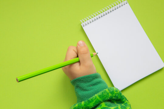 Child's hand on blank notepad with green color pencil