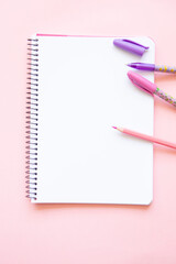 pink pencil and pens on notebook with blank page on pink background