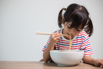 Cute Asian child girl eating delicious instant noodles at home.