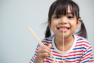 Cute Asian child girl eating delicious instant noodles at home.