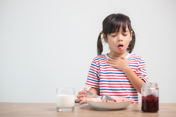 Asian children girls eating bread and desserts and sticking in one's throats with choked food or puke  on the table at home for breakfast or lunch - obrazy, fototapety, plakaty