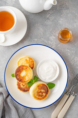 Cottage cheese pancakes, syrniki, ricotta fritters with honey and sour cream on a gray concrete background. Healthy and delicious breakfast. Top view, copy space.