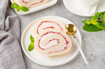 Sponge cake roll with strawberry jam and cream on a white plate on a gray background. Copy space.