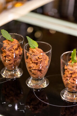 A portrait of a few glass cups full of delicious chocolate mousse with a mint leaf on top of them for some freshness standing on a cooking plate ready to be served and eaten.