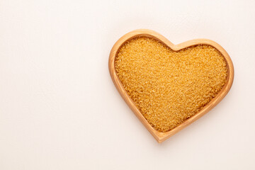 Brown sugar in heart wooden bowl shape on pasttel background.