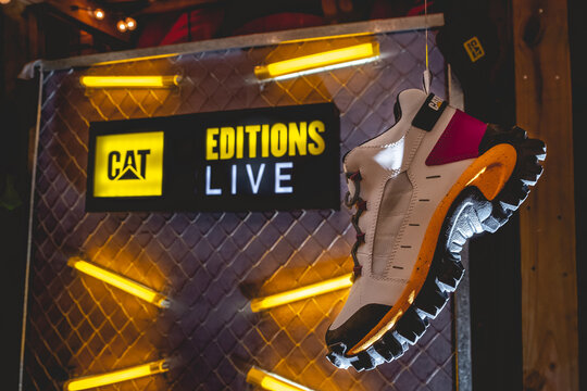 Beautiful 'CAT' Sneaker Hanging In Front Of A Wall Decoration With 'CAT Editions Live' Logo And Yellow Neon Tubes In The Night