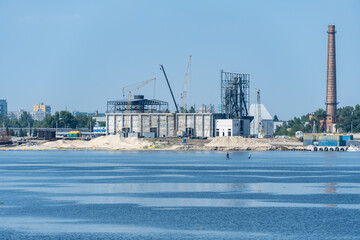 Obraz premium Big port cranes on the river. Extraction and transportation sand. Harbor crane loads water resources into the barge. Special equipment and water transport. River port. Industrial city.