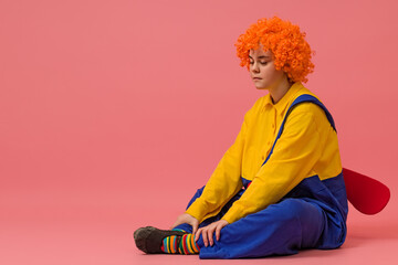 a sad clown in a wig and a yellow-blue suit with a propeller on his back sits on a colored...