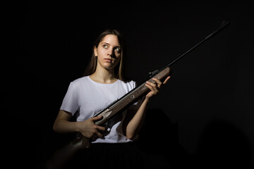 Fototapeta na wymiar young woman with long hair in a white t-shirt with a rifle on a black background