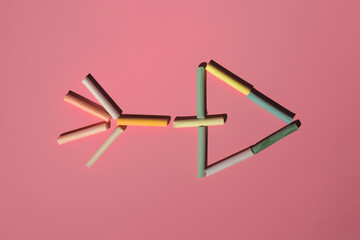colored pastel crayons lie with an arrow on a pink background