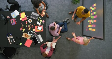 Overhead view of creative team in a meeting brainstorming ideas. Professional colleagues working together to plan a solid marketing strategy. Group in close collaboration inside boardroom - Powered by Adobe