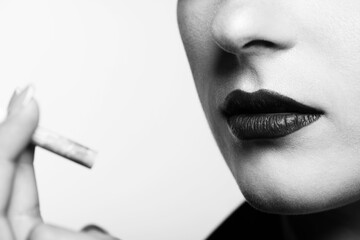 Close-up portrait of woman lips holding cigarette in her hands near face. Selective focus and image with shallow depth of field. White studio background with copy space. Black and white image