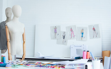 Background of interior tailor shop or room with nobody, there are mannequin, clothes, thread, sewing machine on table and paper of clothing design on wall. Lifestyle and small business concept.