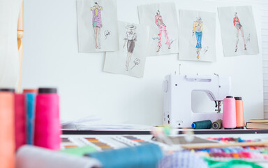 Background of interior tailor shop or room with nobody, there are mannequin, clothes, thread, sewing machine on table and paper of clothing design on wall. Lifestyle and small business concept.