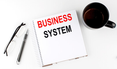 Coffee,glasses,pen and notebook written with BUSINESS SYSTEM , on white background.