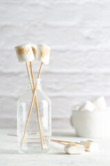 White marshmallows in a bottle and in a white cup, on white background with copy space. 