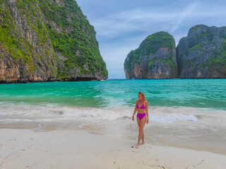 Young blond girl with bikini standing on a sand in front of ocean waves at Maya bay in Thailand