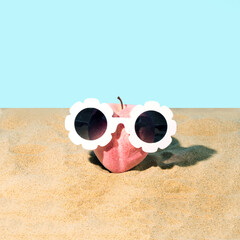 Summer, modern, creative idea of a peach with glasses on the beach in the sand. Sky blue...