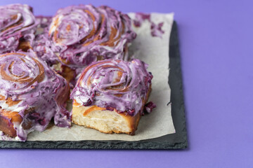Cinnabon buns decorated with cinnamon, pecan and violet cream cheese sauce on a Very Peri color of the year 2022 background. Close up