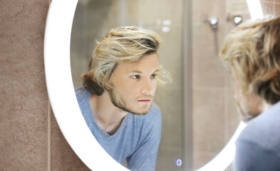 young man looking in the mirror,combing his hair,looking at problems on face.