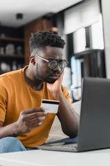 A young black cheerful man paying online with credit card