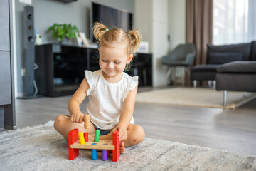 Cute caucasian little girl playing on the floor at home with eco wooden toys. Montessori toy. The...