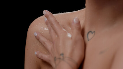 Extreme close-up shot of good-looking young slim white-skinned woman strokes her wet clavicle on black background | Skin hydration concept