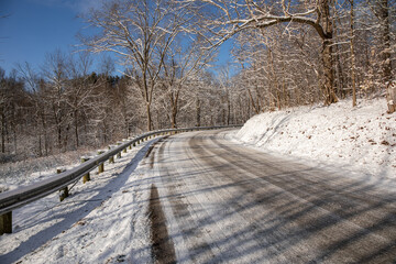 Obraz premium Winding snowy country road through the bare trees in winter in Holmes County